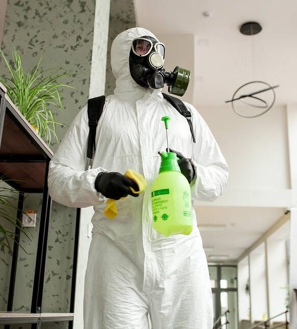 Technician in full protective gear disinfecting an office